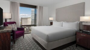Habitación de hotel con una cama grande, un escritorio con silla, una ventana con cortinas y vistas a la ciudad.