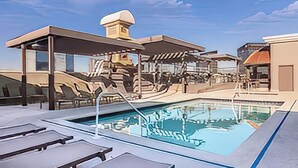 Un área de piscina moderna con sillones de descanso, una fuente de agua y fachada de piedra.