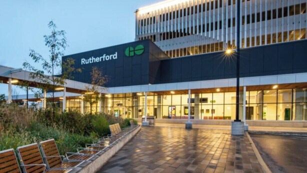 A modern building with a sign reading "Rutherford" and a covered outdoor seating area with benches.