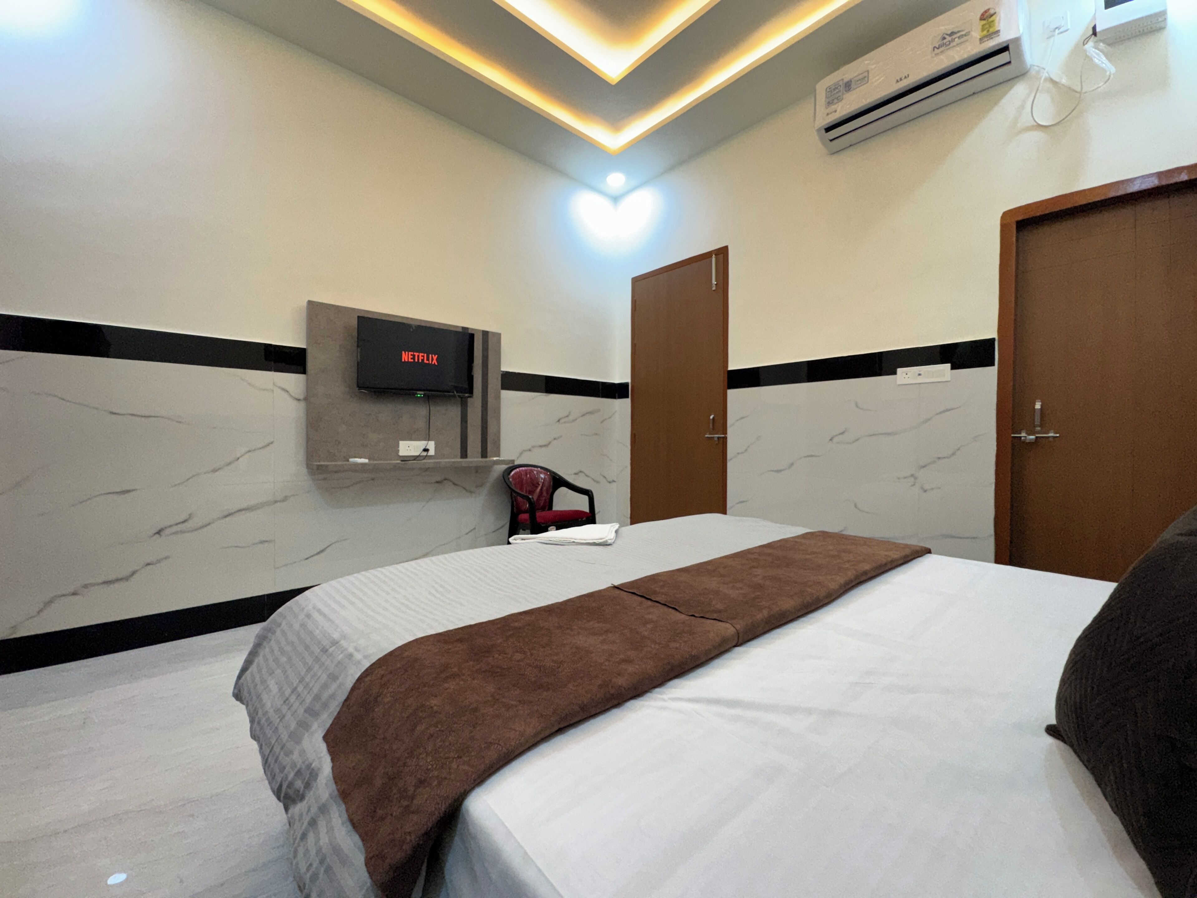 A hotel room with a bed, a TV mounted on the wall, a chair, and a door.