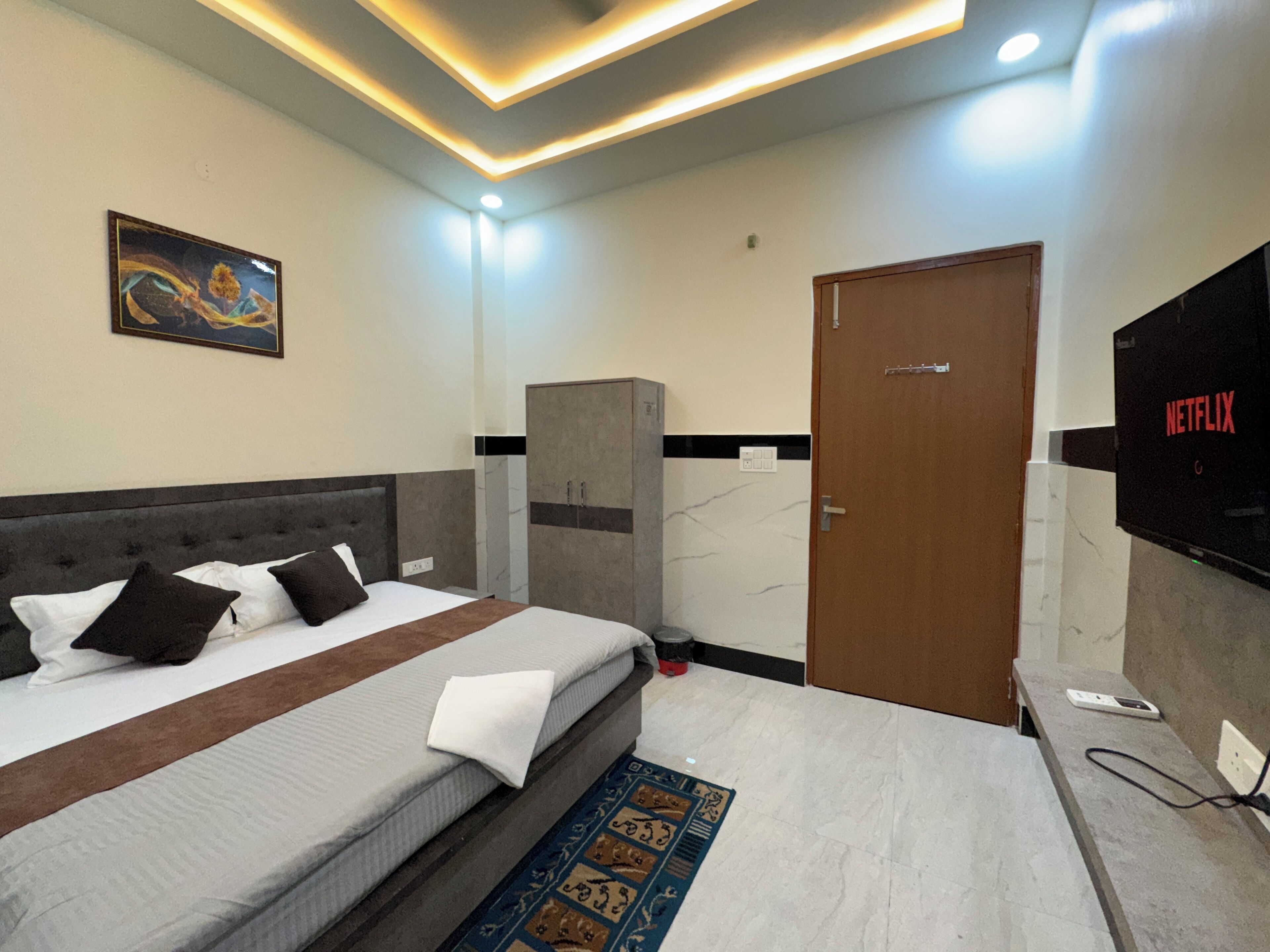 A hotel room with a bed, a wardrobe, a television, and a painting on the wall.