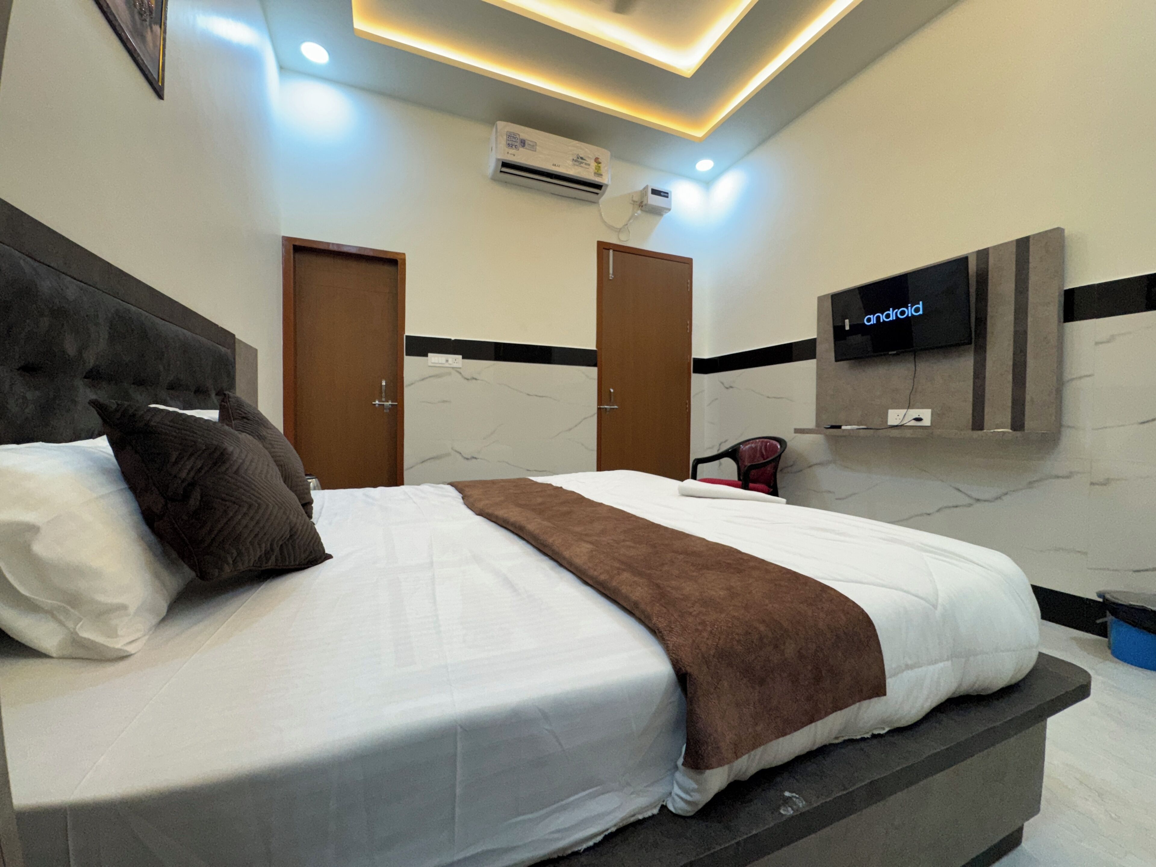 A modern hotel room with a large bed, a TV mounted on the wall, and an air conditioning unit.