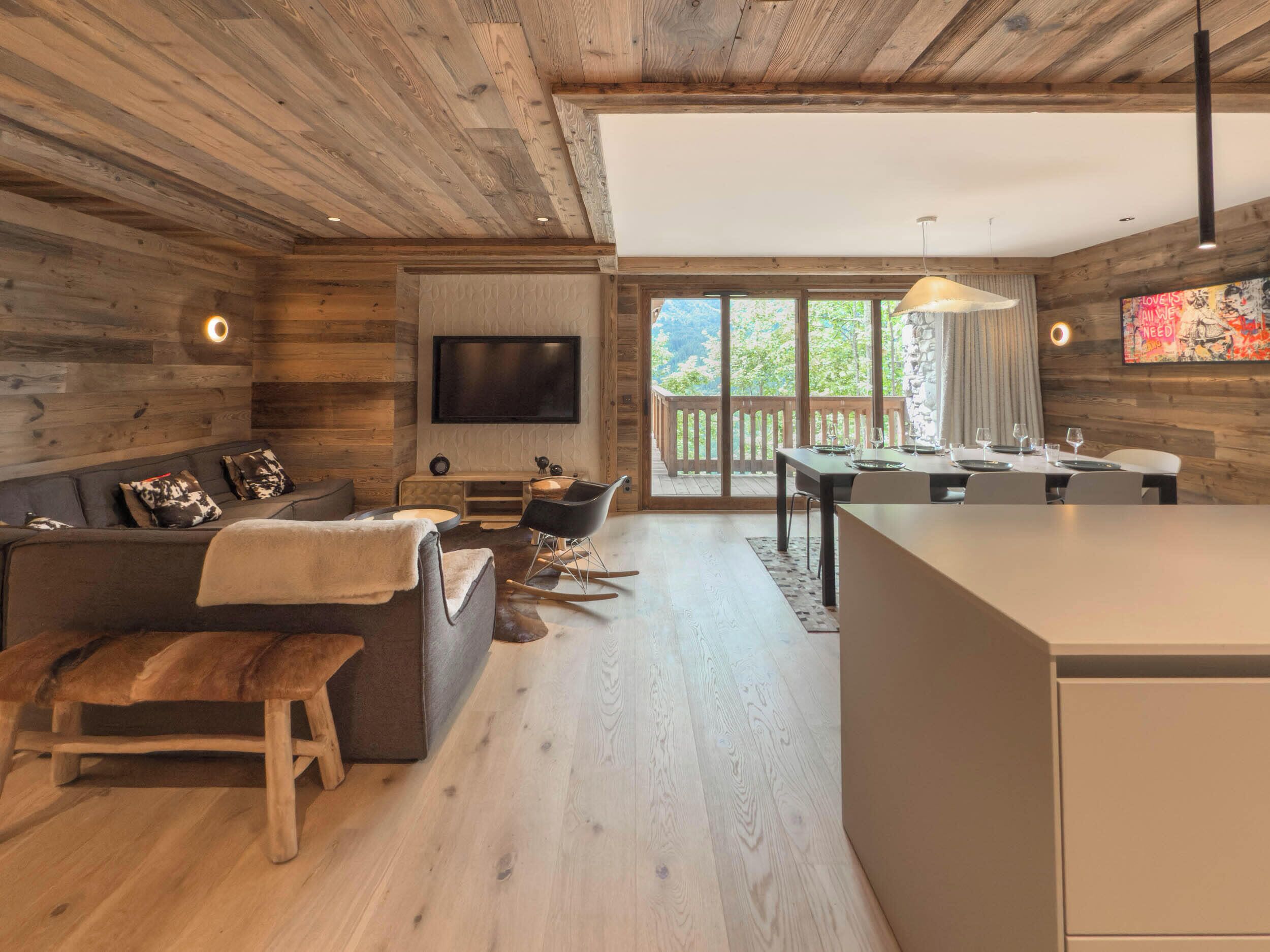 A modern interior with a wooden ceiling, a flat-screen TV, a dining area, and a kitchen.