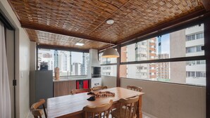 Comedor con mesa y sillas de madera, lámpara colgante y vistas de la ciudad a través de grandes ventanales.