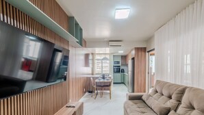 Una cocina moderna con televisor integrado, un comedor con mesa y sillas, y una sala de estar con sofá.