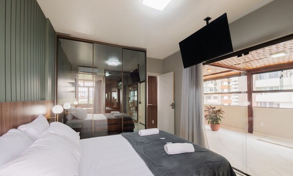 A modern hotel room with a large bed, a TV, and a balcony with a view of the city.