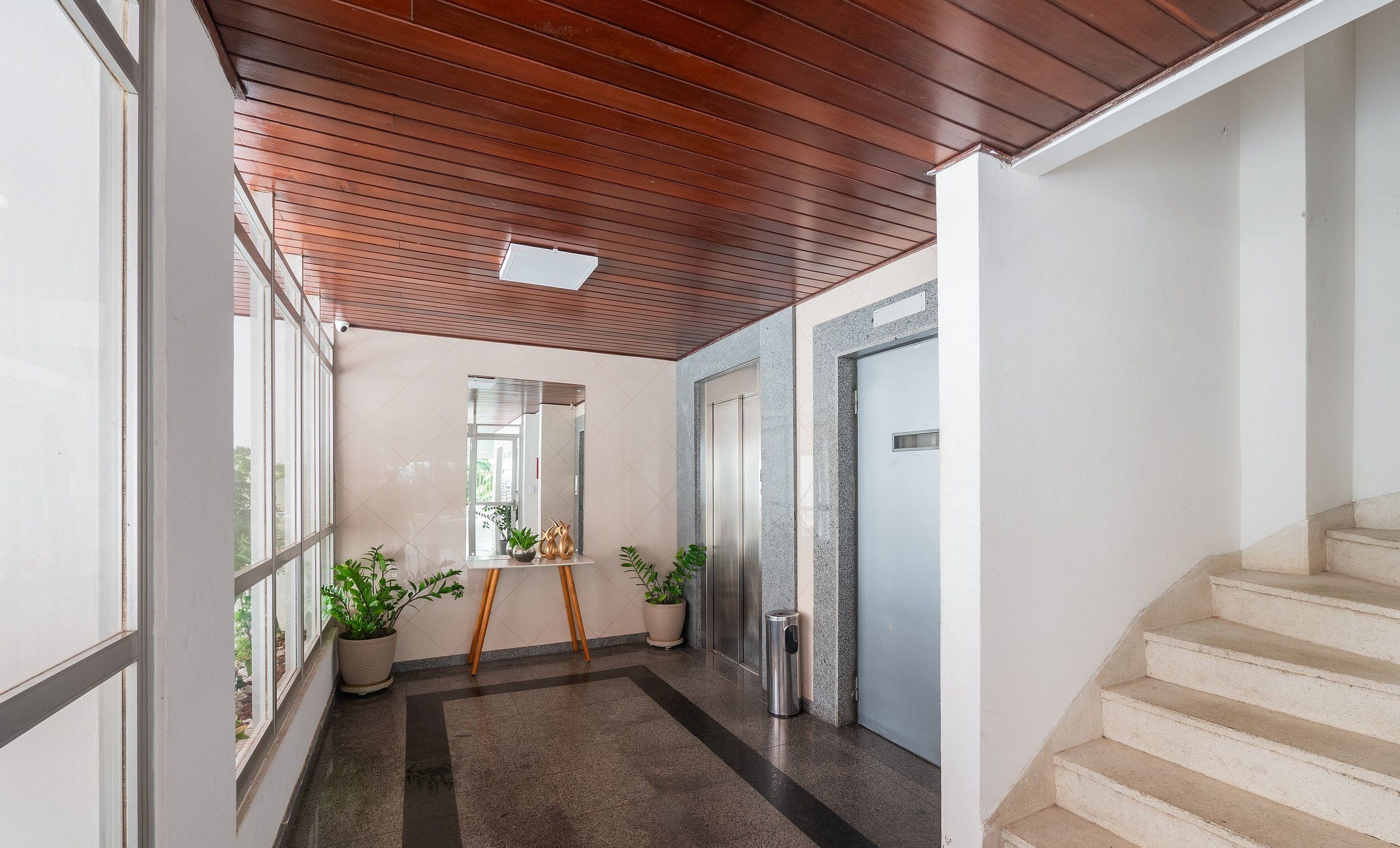 Un couloir avec un plafond en bois, une plante en pot, une poubelle et un escalier.