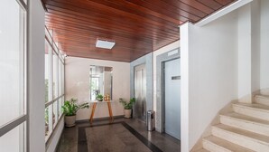 Un pasillo con techo de madera, una planta en maceta, un cubo de basura y una escalera.