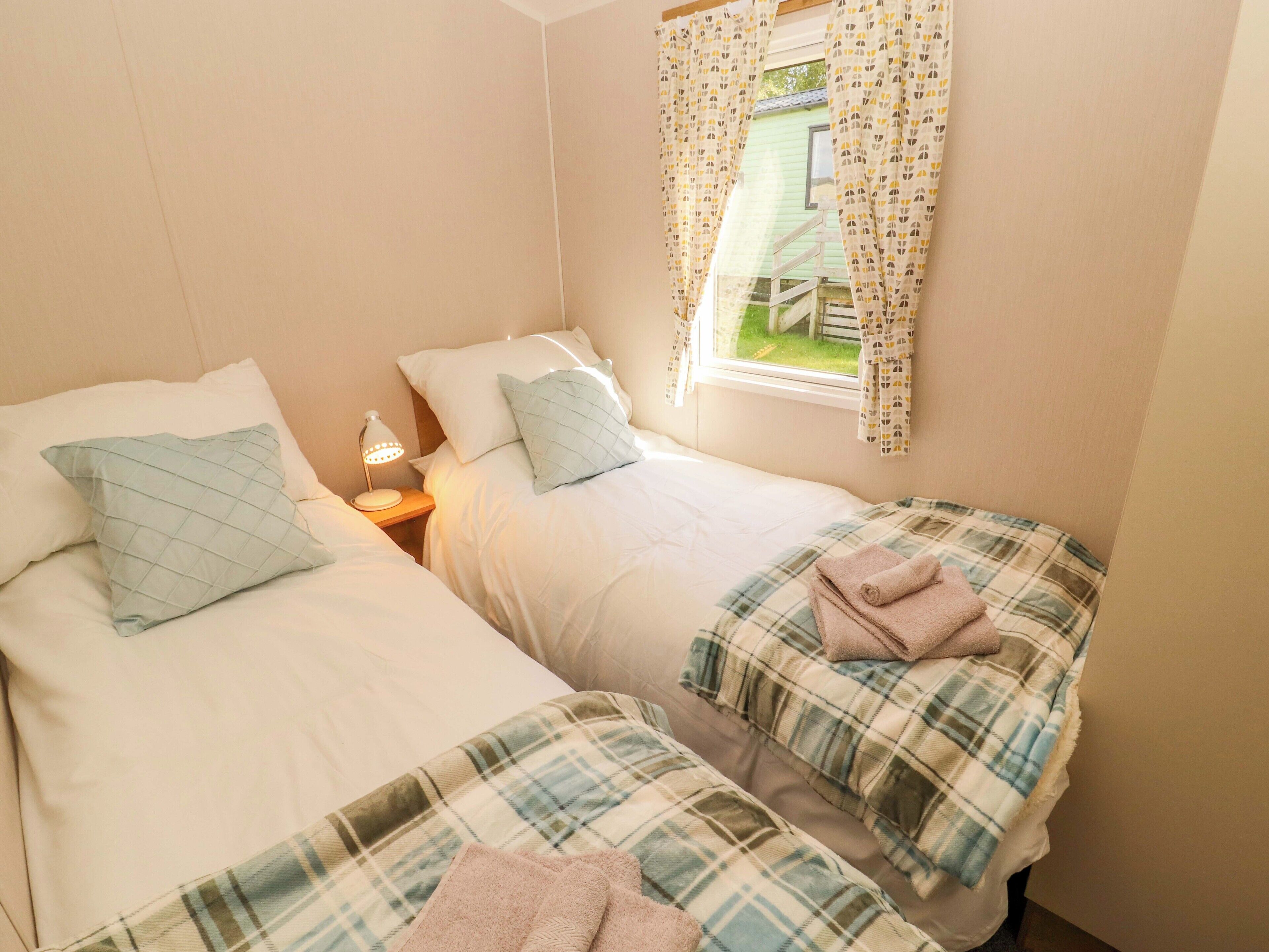 A bedroom with two beds, a nightstand with a lamp, and a window with curtains.