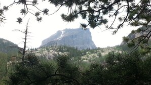 A mountainous landscape with a prominent rocky peak, surrounded by dense forest and a body of water.