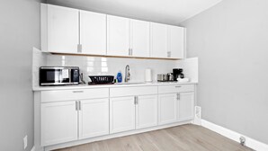 A modern kitchen with white cabinets, a microwave, a coffee maker, and a sink.