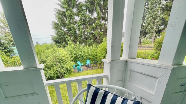 Una silla de mimbre blanca con un cojín azul y blanco a rayas sobre una terraza verde.