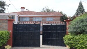 Een omheinde oprijlaan naar een huis met een pannendak en een bakstenen muur.