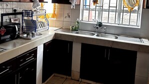 Een keuken met donkere kastjes, een spoelbak, een raam met gele gordijnen en een betegelde vloer.
