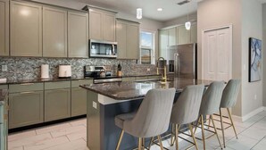 A modern kitchen with a central island, bar stools, and built-in appliances. - Star Wars Theater & Pool Paradise near Disney (Kissimmee)