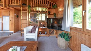 Ein Holzblock-Interieur mit Fernseher, weißem Sofa, Holzregalen und einem großen Fenster.