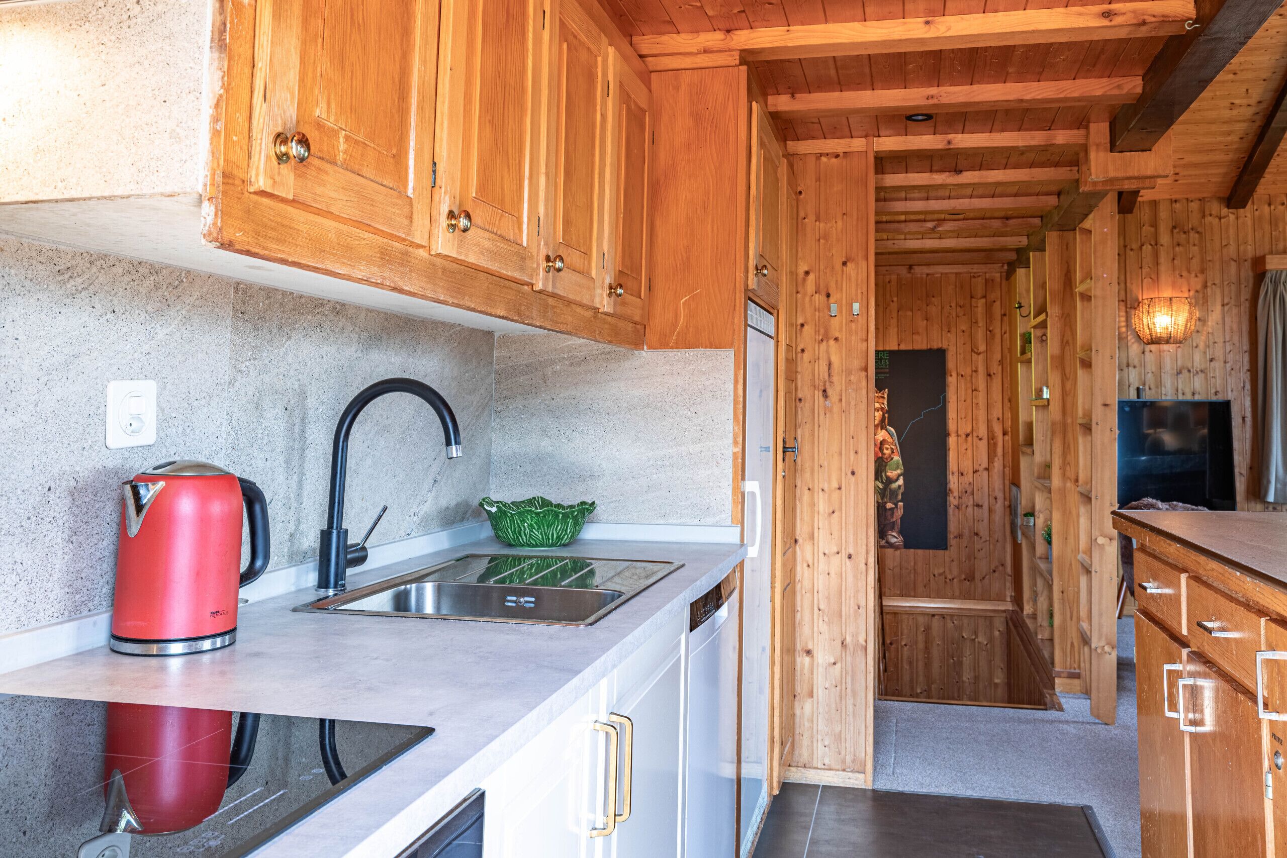 A modern kitchen with wooden cabinets, a stainless steel sink, and a red kettle.