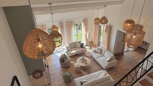 Un salon spacieux avec un grand canapé blanc, une table basse ronde et plusieurs lampes suspendues en osier.