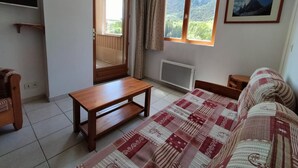 A room with a bed, a wooden table, a radiator, and a window with a view of mountains.