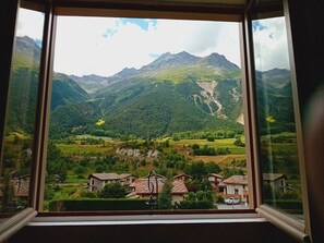 Vista da janela sobre um vale com montanhas, casas e uma estrada.