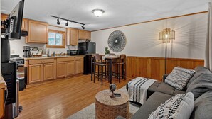 Eine moderne Küche mit Holzschränken, ein Essbereich mit rundem Tisch und ein gemütliches Wohnzimmer mit Sofa und Lampe.