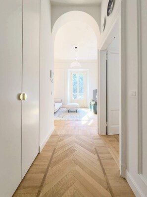 Un pasillo con piso de espiga que conduce a una habitación con ventana, un sofá y una pequeña mesa.