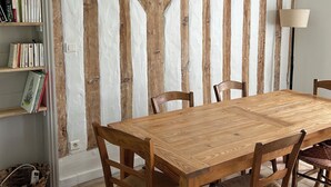 A dining area with a wooden table and chairs, a bookshelf, and a wall with exposed wooden beams. - Traditional Landes house for rent (Lévignacq)