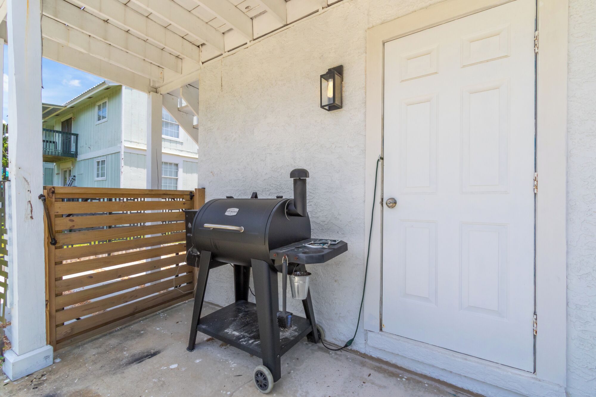 A barbecue grill outside a building with a white door and a wooden gate.