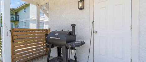 A barbecue grill outside a building with a white door and a wooden gate.