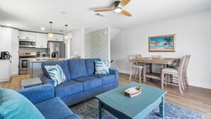 A modern living room with a blue sofa, a teal coffee table, and a dining area with wooden chairs.