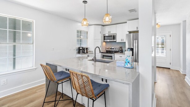A modern kitchen with white cabinetry, stainless steel appliances, a large island with bar stools, and pendant lighting.