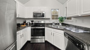 Cocina moderna con armarios blancos, electrodomésticos de acero inoxidable, encimera de granito y ventana con vistas.