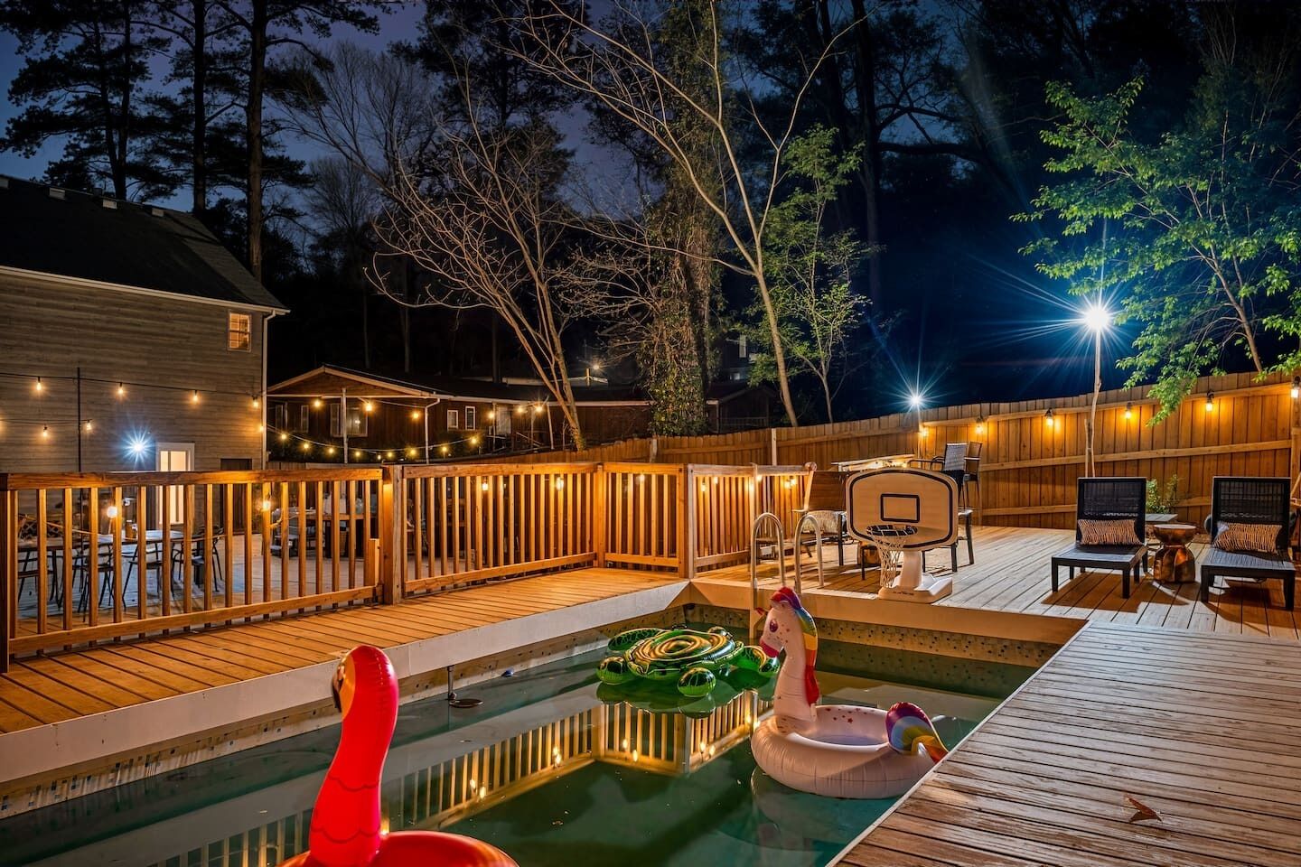 A backyard with a swimming pool, deck chairs, and a basketball hoop.