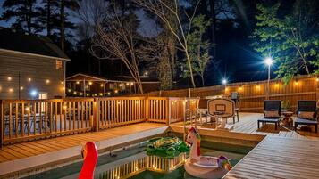A backyard with a swimming pool, deck chairs, and a basketball hoop.