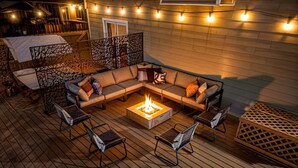 Terraza exterior con fogata, zona de estar y luces colgantes.