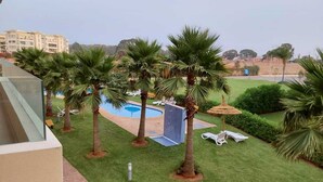 Un área de piscina con palmeras, sillas de descanso y un edificio al fondo.