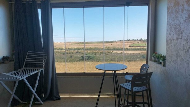 Un balcón con una mesa y dos sillas, vistas a un paisaje árido y una cortina.