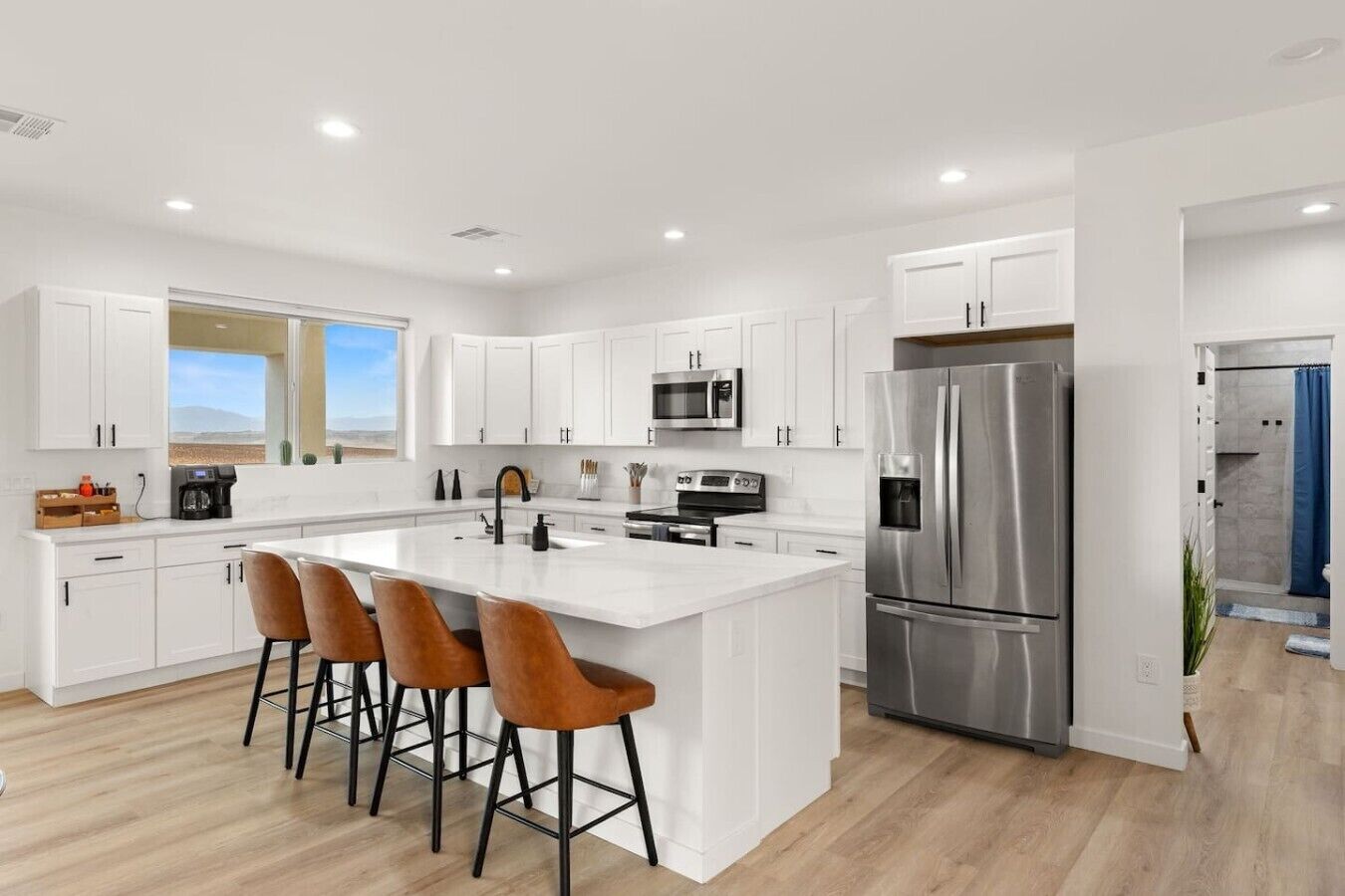 A modern kitchen with white cabinetry, a stainless steel refrigerator, and a central island with bar stools.