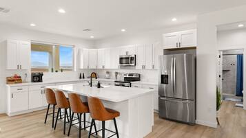 A modern kitchen with white cabinetry, a stainless steel refrigerator, and a central island with bar stools.