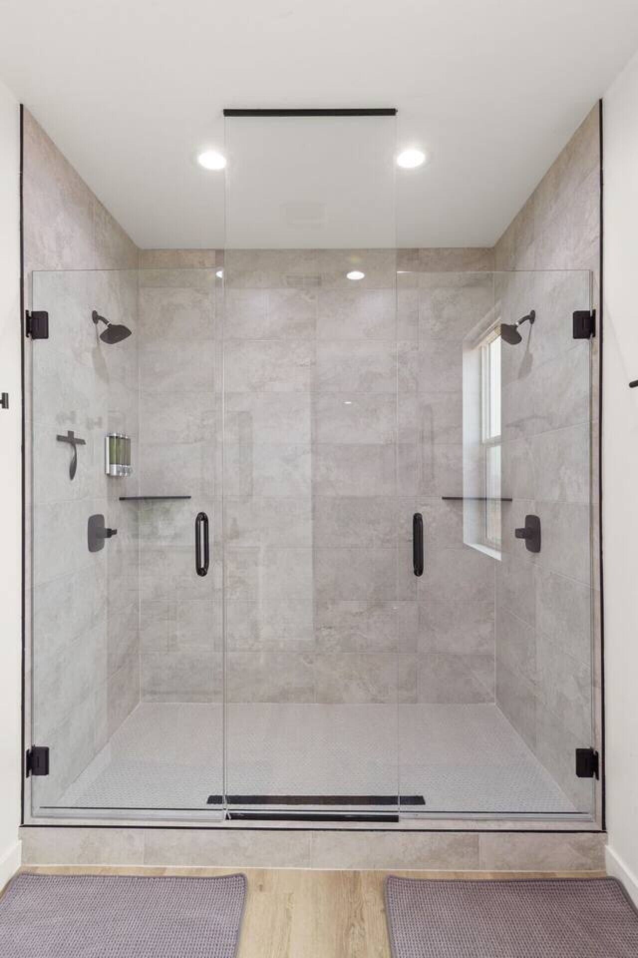 Een moderne douchecabine met glazen deuren, een handdouche, een handmassageapparaat en een klein plankje.