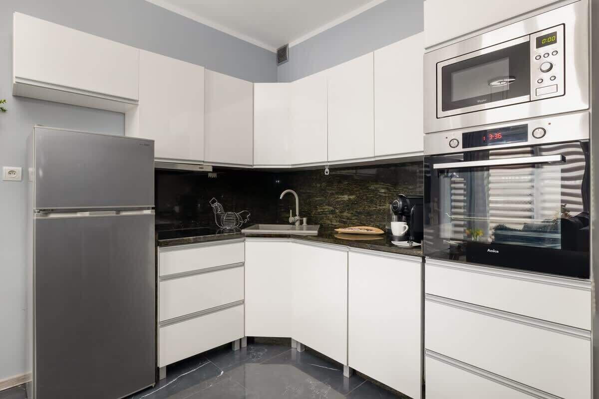 Een moderne keuken met witte kastjes, een roestvrijstalen koelkast, een magnetron en een oven.