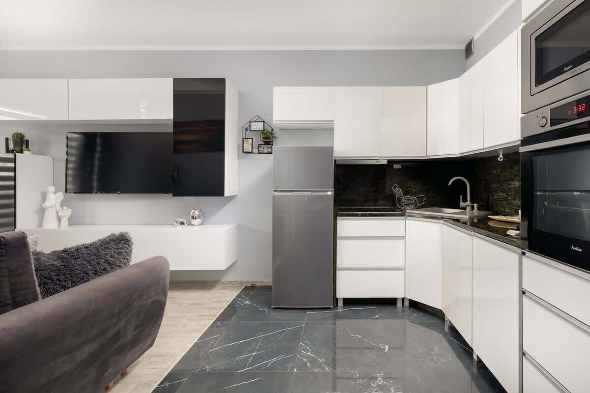 Eine moderne Küche mit weißen Schränken, einem schwarzen Kühlschrank und einem eingebauten Backofen.