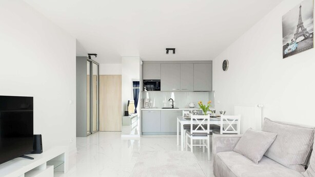 A modern living room with a flat-screen TV, a sofa, and a dining area with a table and chairs.