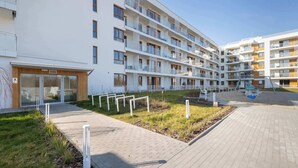 A multi-story residential building with balconies, a paved walkway, and a small garden area.