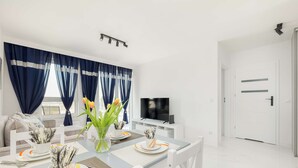 A modern living room with a dining area, white furniture, a flat-screen TV, and a door leading to another room.