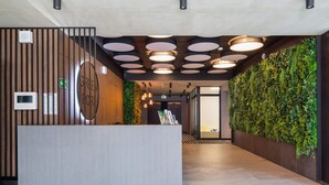Modernilla designilla varustettu vastaanottotiski, viherseinä, jossa on kasveja, ja pyöreillä valaisimilla koristeltu katto.