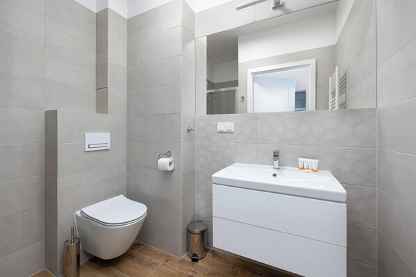 A modern bathroom with a toilet, sink, mirror, and a trash bin.