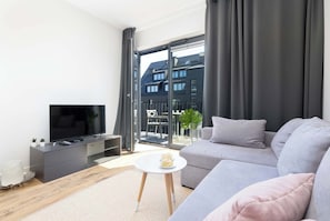 A modern living room with a flat-screen TV, grey sofa, and a small white table.
