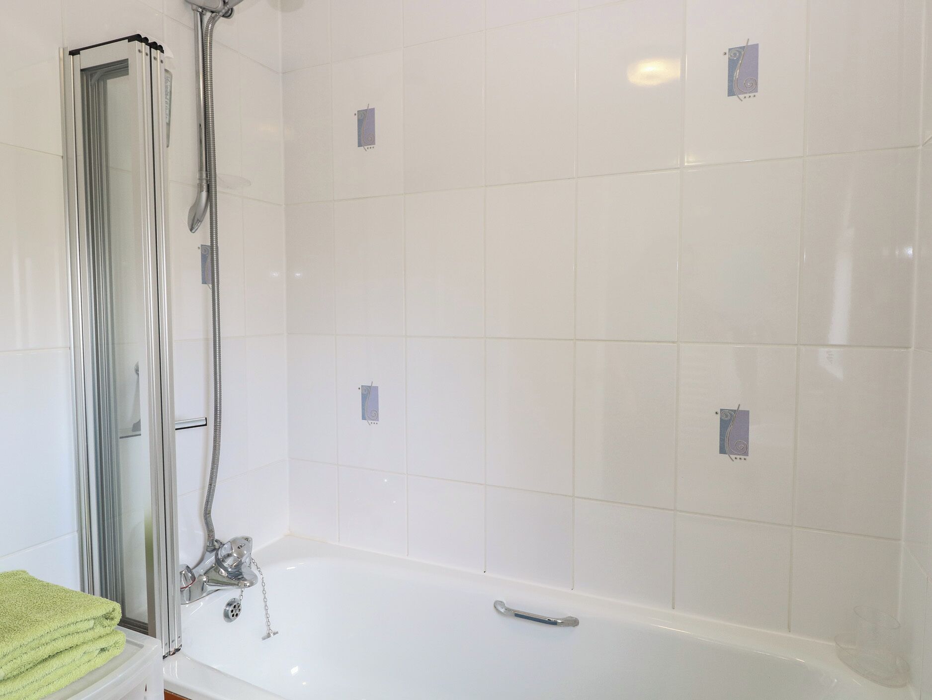 Un baño con ducha envuelta en vidrio, una bañera blanca y una toalla verde sobre un estante blanco.