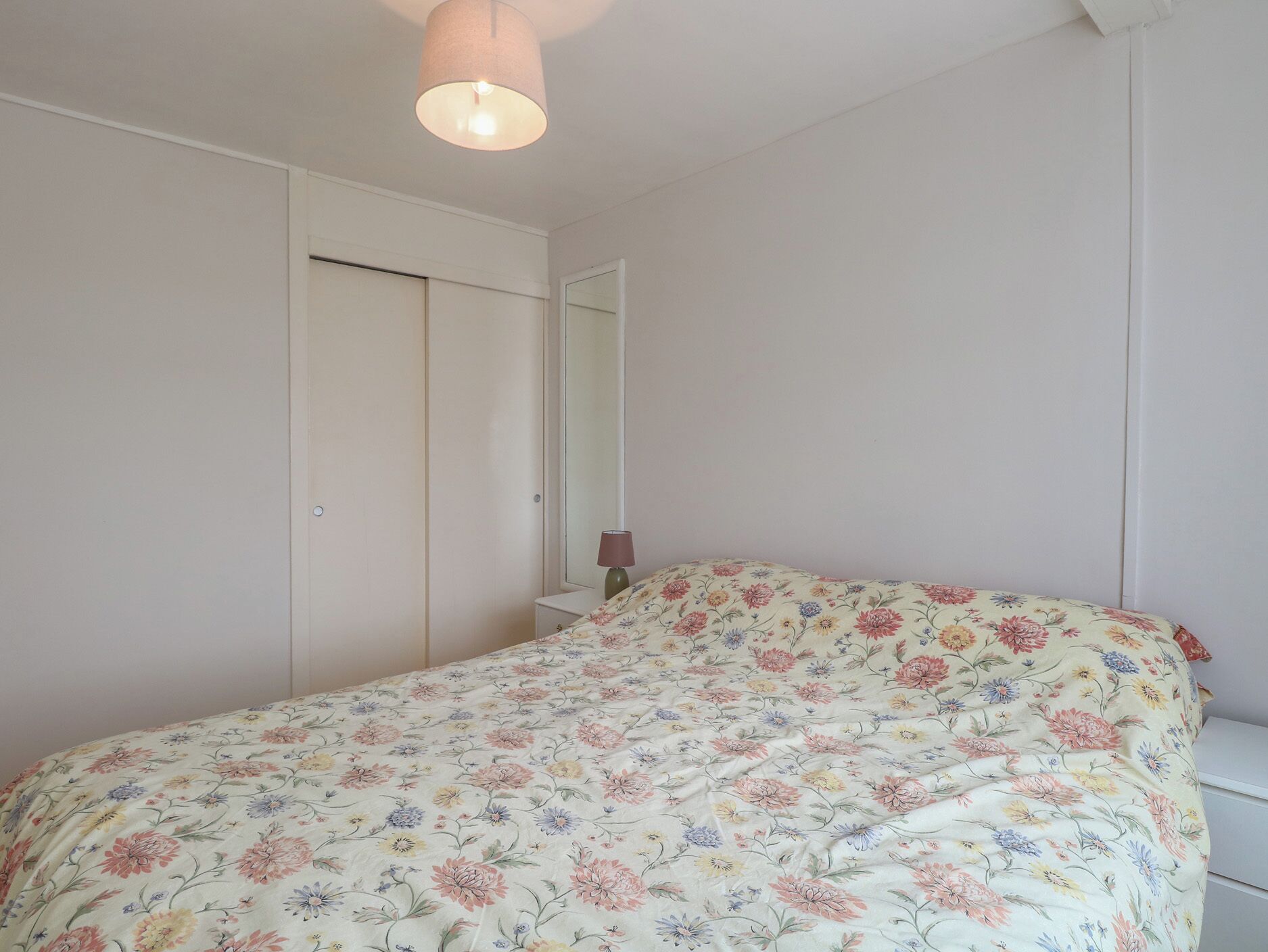 A bedroom with a bed, a nightstand, a mirror, and a door.